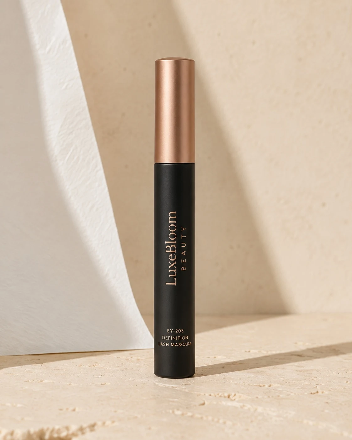 A matte tube of Definition Lash Mascara, upright, front view on a pale sand background.